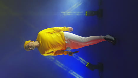 Vertical-video.-A-singer-in-a-yellow-suit-dances-and-sings-with-a-microphone-in-neon-color.-Jump-and-move-vigorously.